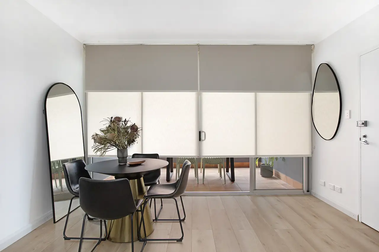 Dual roller blinds on wide sliding door to a balcony in a dining room with a small round black table and 4 black chairs