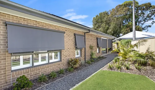 Retractable outdoor blinds on a brick home exterior with landscaped garden