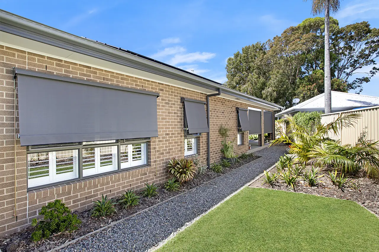 Retractable outdoor blinds on a brick home exterior with landscaped garden
