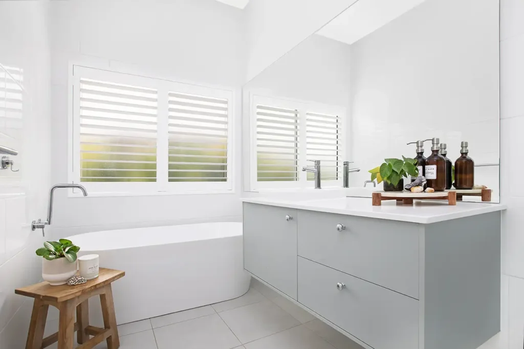 White Plantation Shutters in bathroom with white bathtub and grey benchtop with a white basin
