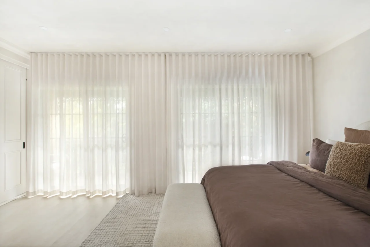 sheer curtains in wave fold across full-width windows in light-filled Sydney bedroom with neutral bedding